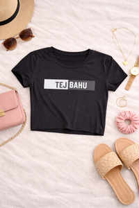 Black t-shirt with 'TEJ BAHU' text on a light surface with accessories around