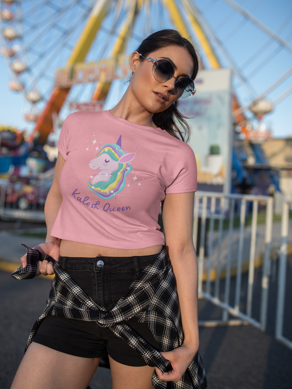 Woman wearing a pink t-shirt with a unicorn design and text, standing in front of a Ferris wheel.